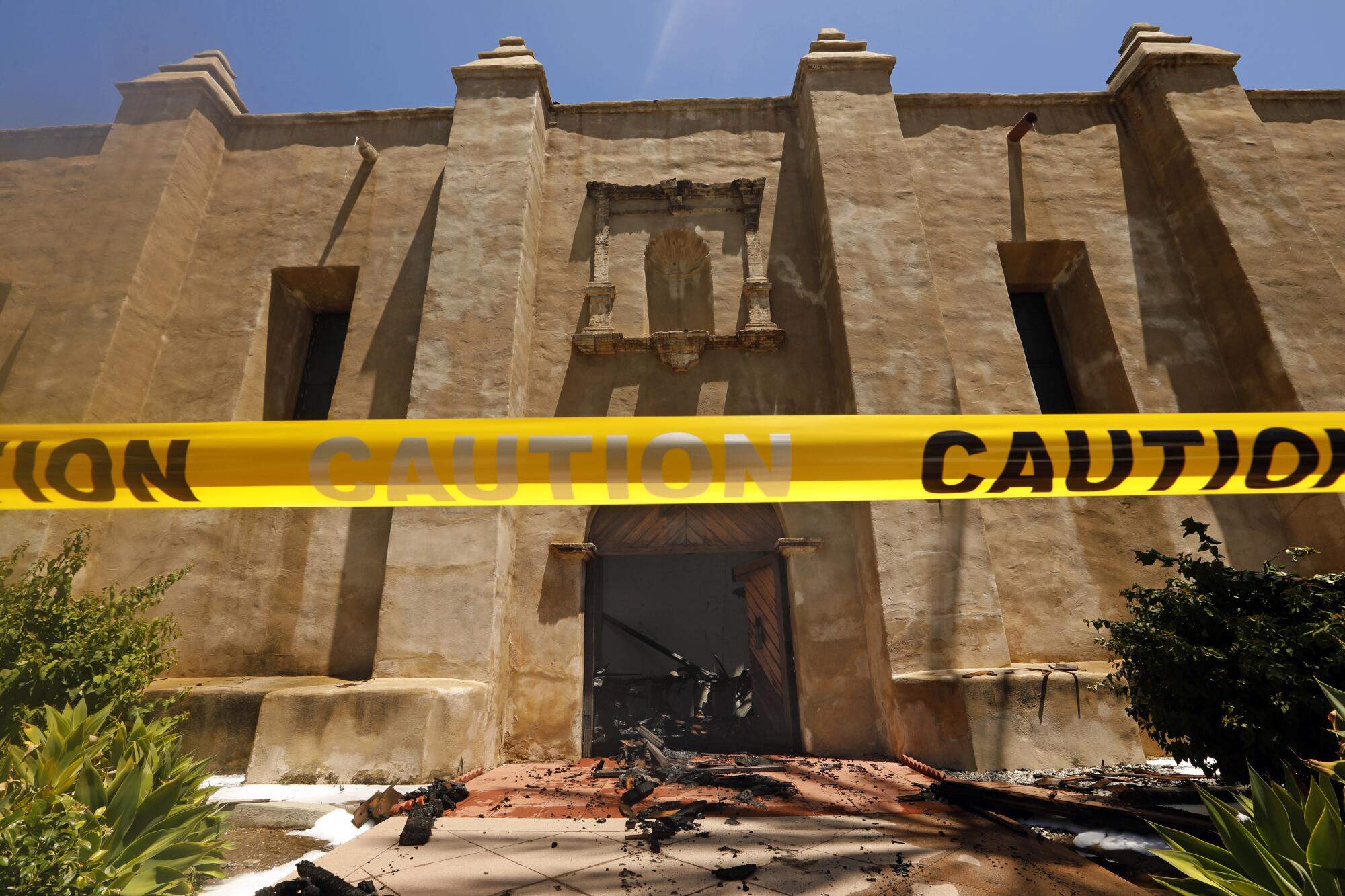 Caution tape in front of a door of the San Gabriel Mission, with burned debris scattered in front of the door