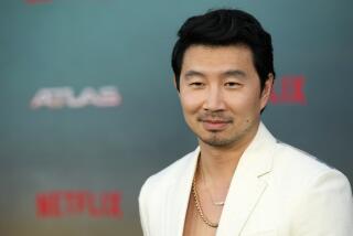 Simu Liu poses in a white suit and gold chain necklaces at the May 2024 Netflix premiere of "Atlas" at the Egyptian Theatre