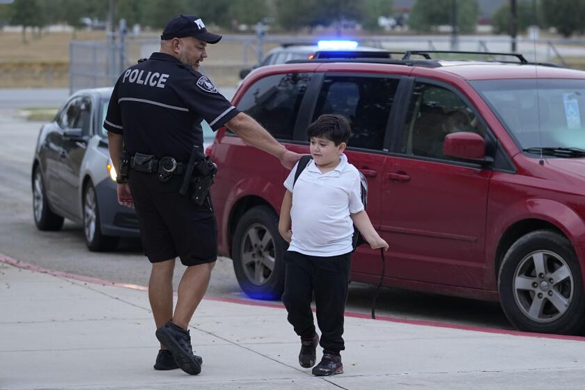 El agente Ruben Cardenas, del Distrito Escolar Independiente del Sur, a la izquierda, saluda a un chico que llega a la Escuela Primaria Freedom, el miércoles 23 de agosto de 2023, en San Antonio, Texas. (AP Foto/Eric Gay)