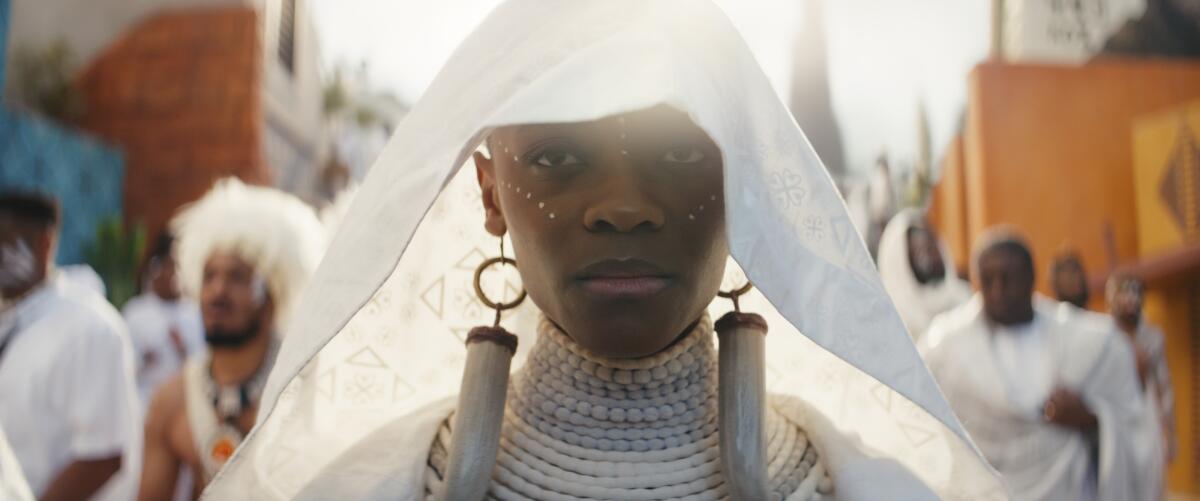 A woman dresses all in white, including large earrings and a beaded neck collar in "Wakanda Forever."