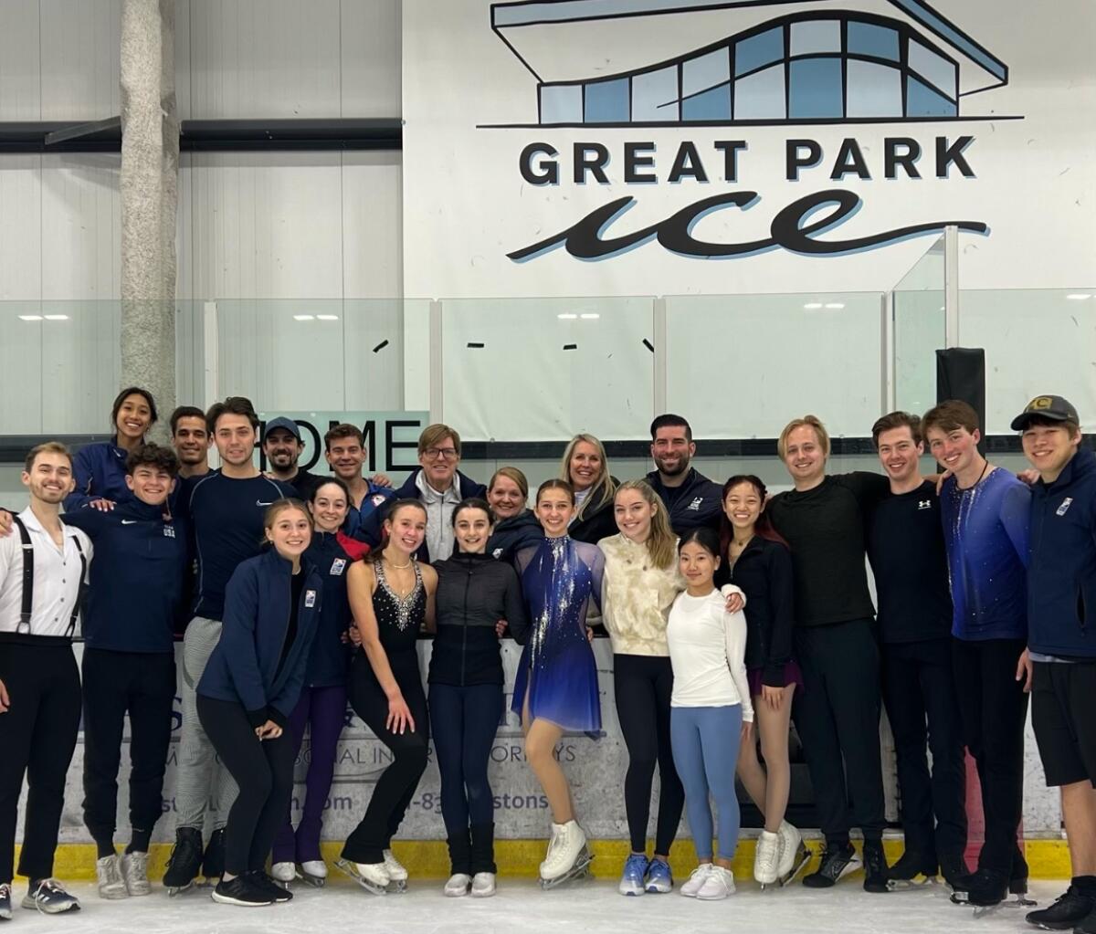 Тодд Сэнд и Дженни Мено позируют для фото со многими фигуристами, которые тренируются на льду Great Park Ice.
