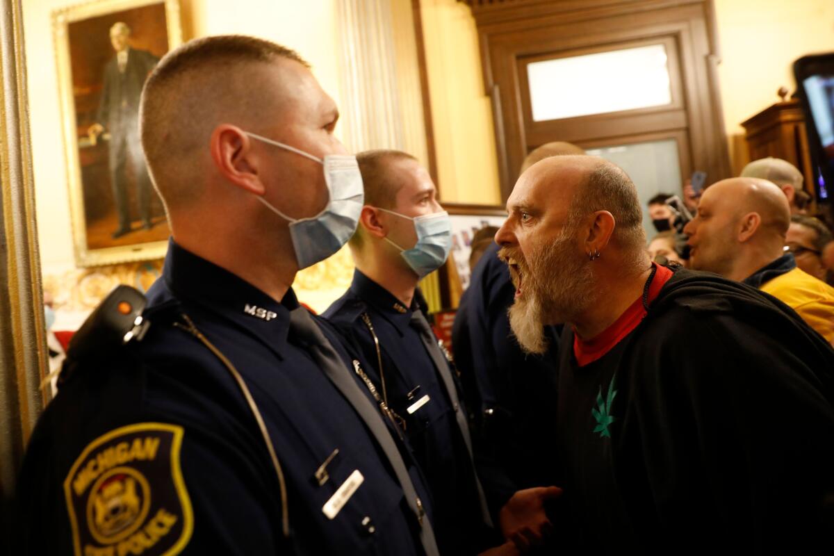 A maskless man screams in the faces of masked police officers standing in a line