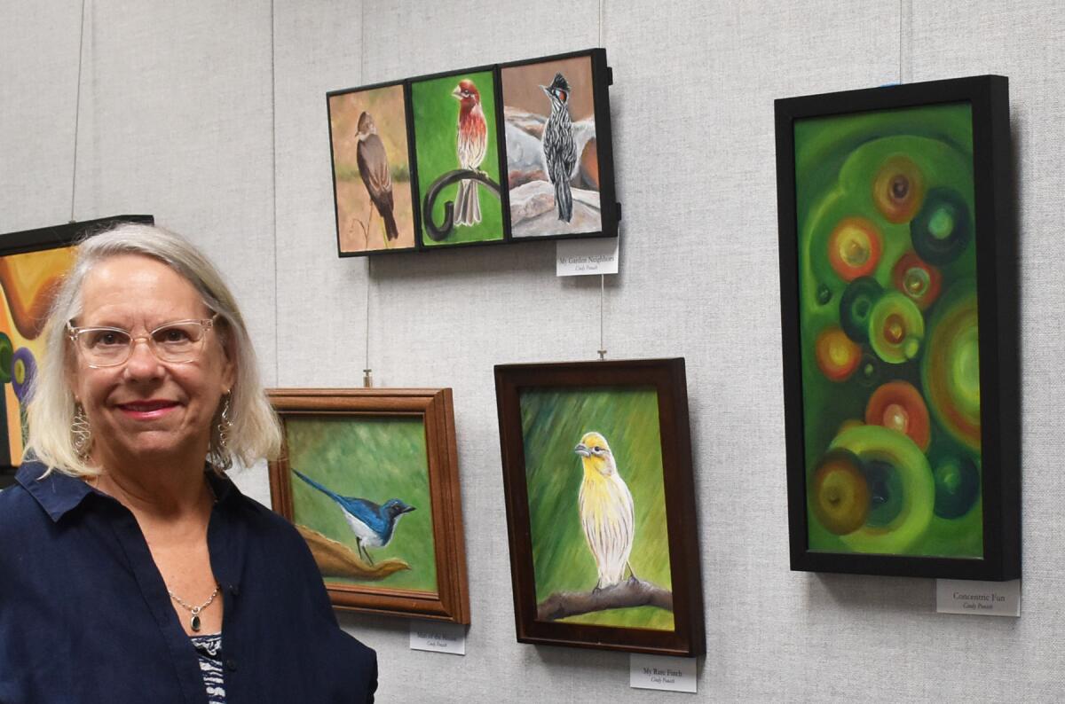 Cindy Ponath next to her oil paintings of birds and one of her abstracts titled “Concentric Fun” on display at the RB Library