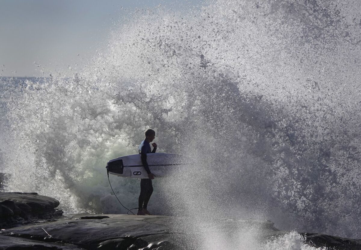 Waves crash against the rocks in La Jolla as a surfer waits to head out during a king tide.