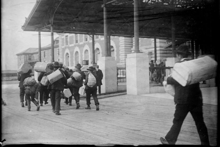 Immigrants carrying luggage, Ellis Island, New York, Date unknown.