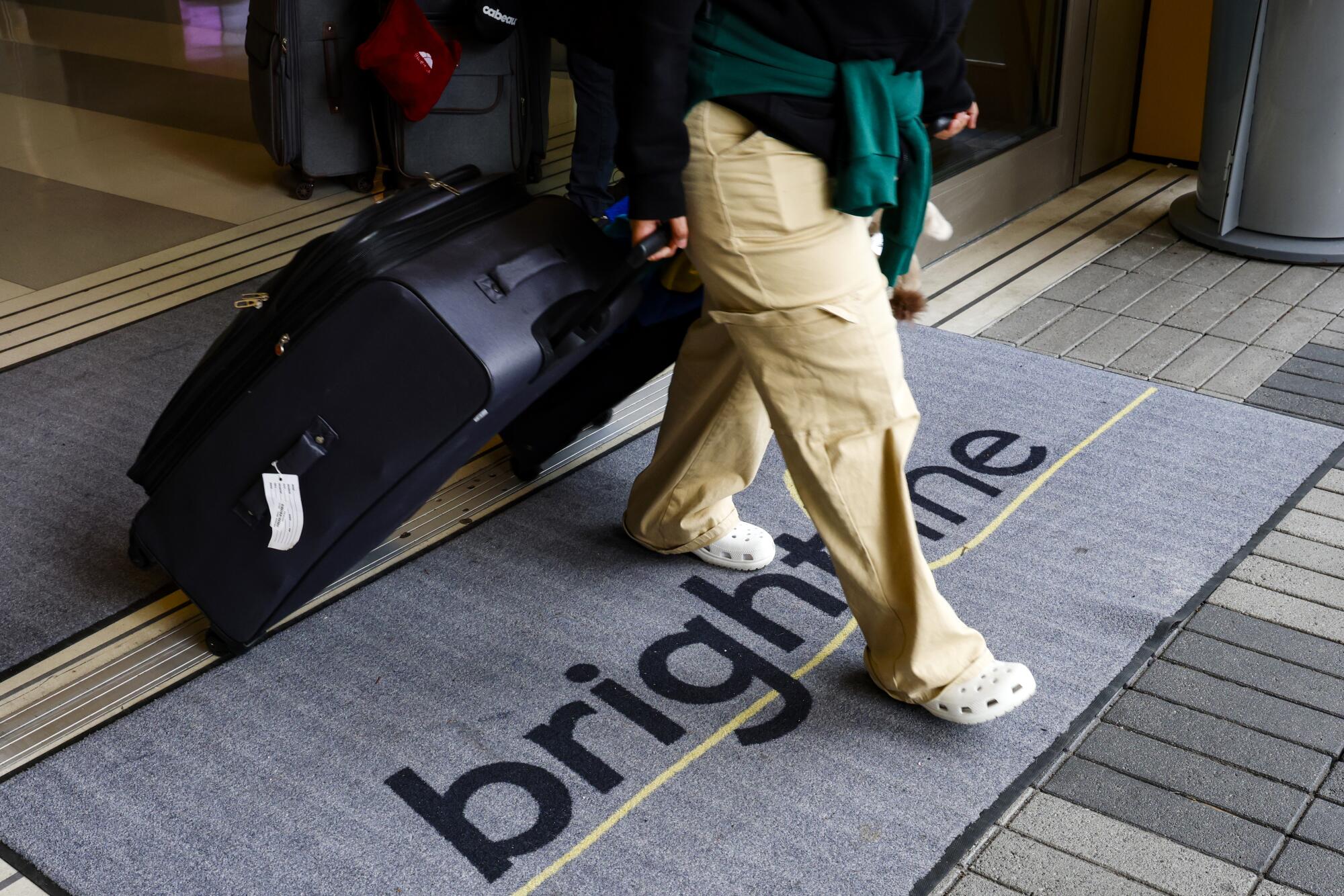 A person carrying luggage walks through a doorway and over a gray mat that says "brightline" in dark letters