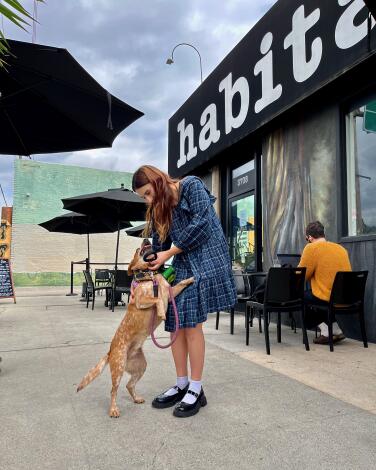 A woman pets her dog as it playfully jumps on her in front of Habitat Coffee Shop.