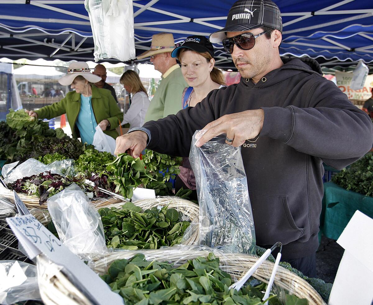 Carlo Micalizio, right, and his wife Amy, left, of La Cañada Flintridge, grab spinach and other greens at the La Cañada Flintridge Farmers Market on Saturday, March 16, 2013. The farmers market will be relocated to Memorial Park for at least three months as the city resurfaces and makes improvements to the current site.