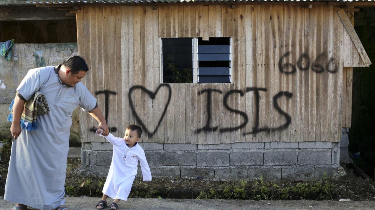 A man and his son head to Eid al-Fitr prayers in June, past a sign proclaiming "I love ISIS" that was left behind by Islamic extremists who took over Marawi more than a year ago.