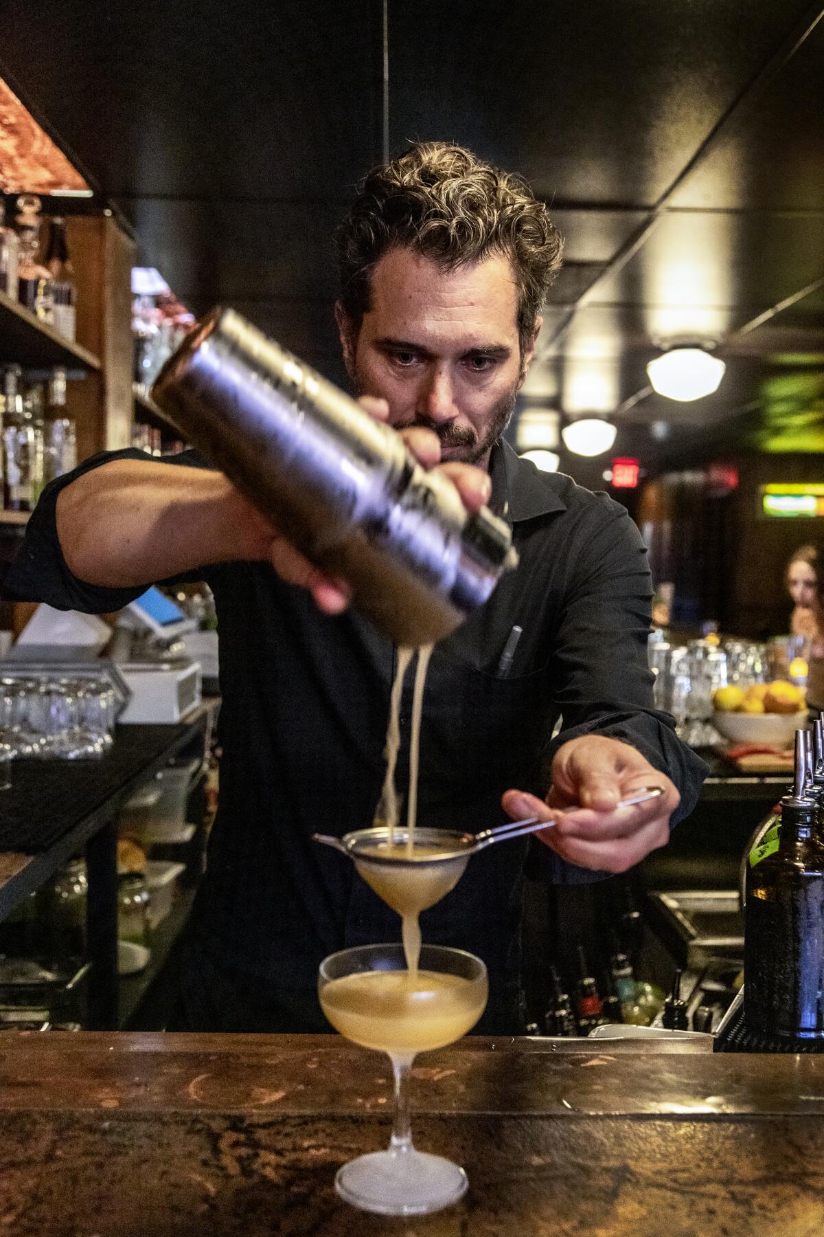 A man strains a drink into a glass.