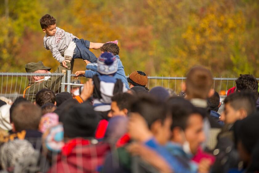An Austrian soldier passes a child over a fence as migrants and refugees cross the Slovenian-Austrian border Oct. 25 in Sentilj.