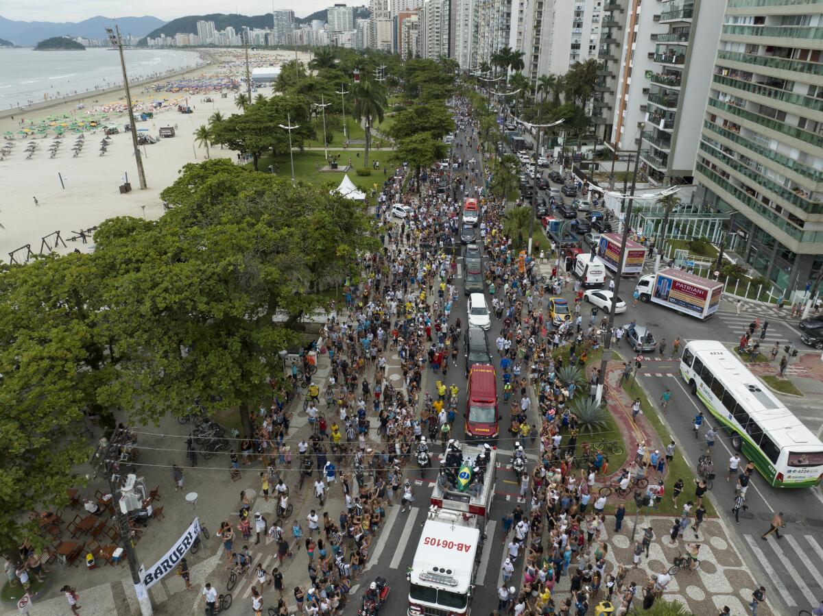 Overhead view of multitudes following a casket during a funeral procession on a seaside thoroughfare 