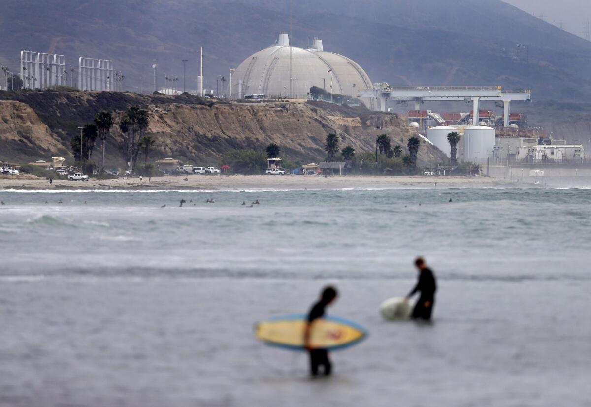 Surfers wade in front of the closed San Onofre nuclear power plant. Southern California Edison, one of the two utilities that owns the plant, wants state regulators to keep a settlement agreement in place that leaves customers on the hook for $3.3 billion of the $4.7-billion cost to close the facility.