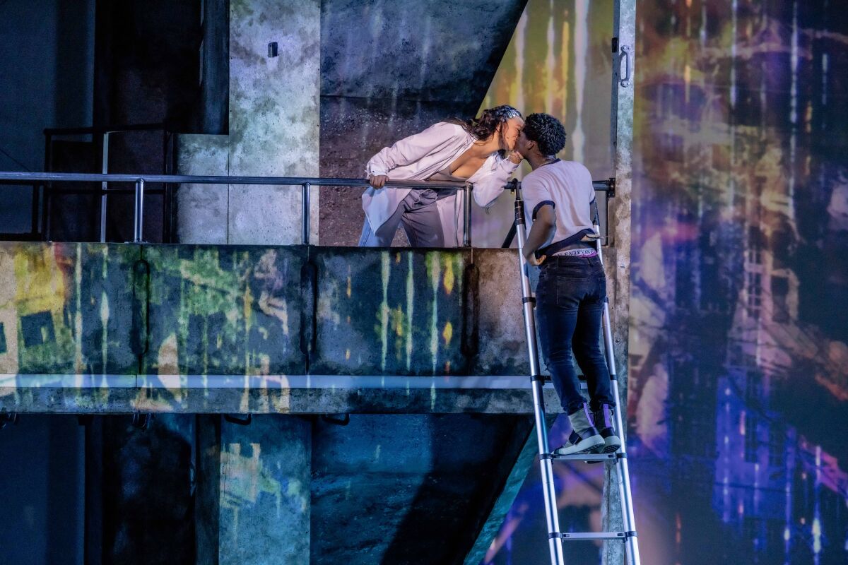 A woman on a balcony and a man on a ladder kiss onstage.