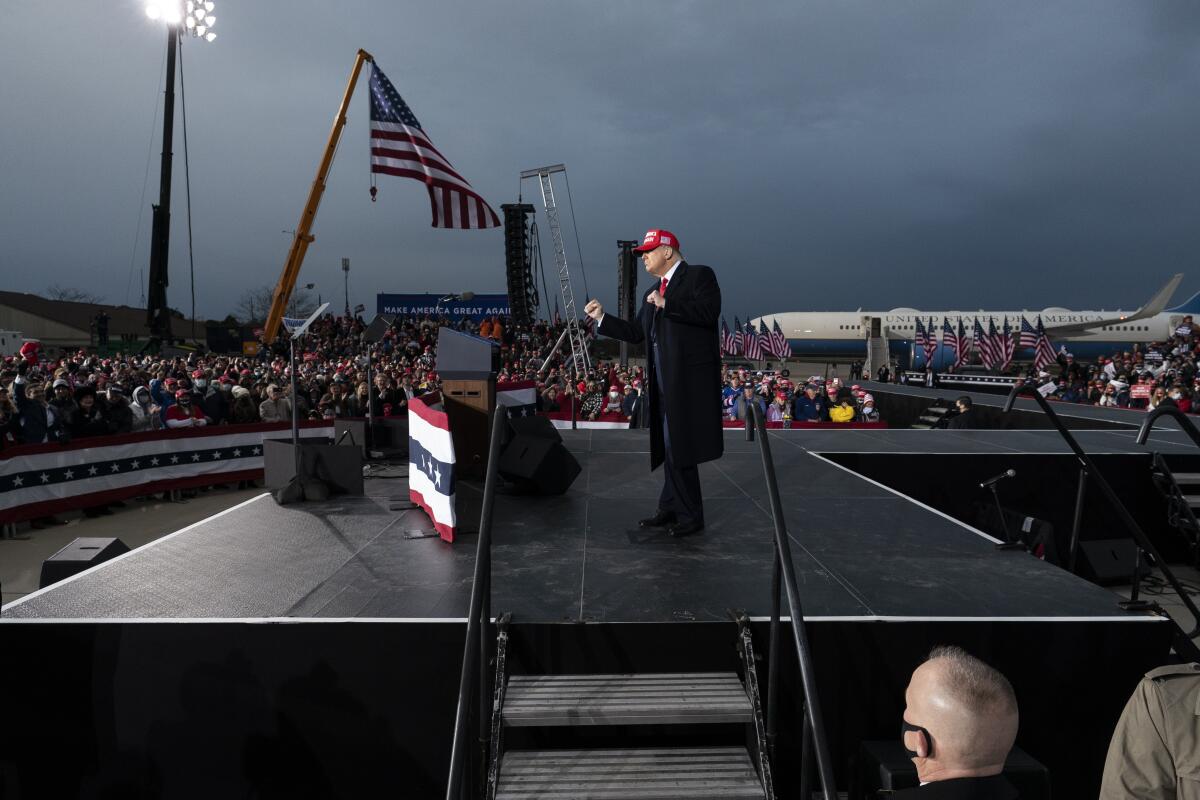 Trump pumps his fists on an outdoor stage at a rally in front of Air Force One under cloudy skies
