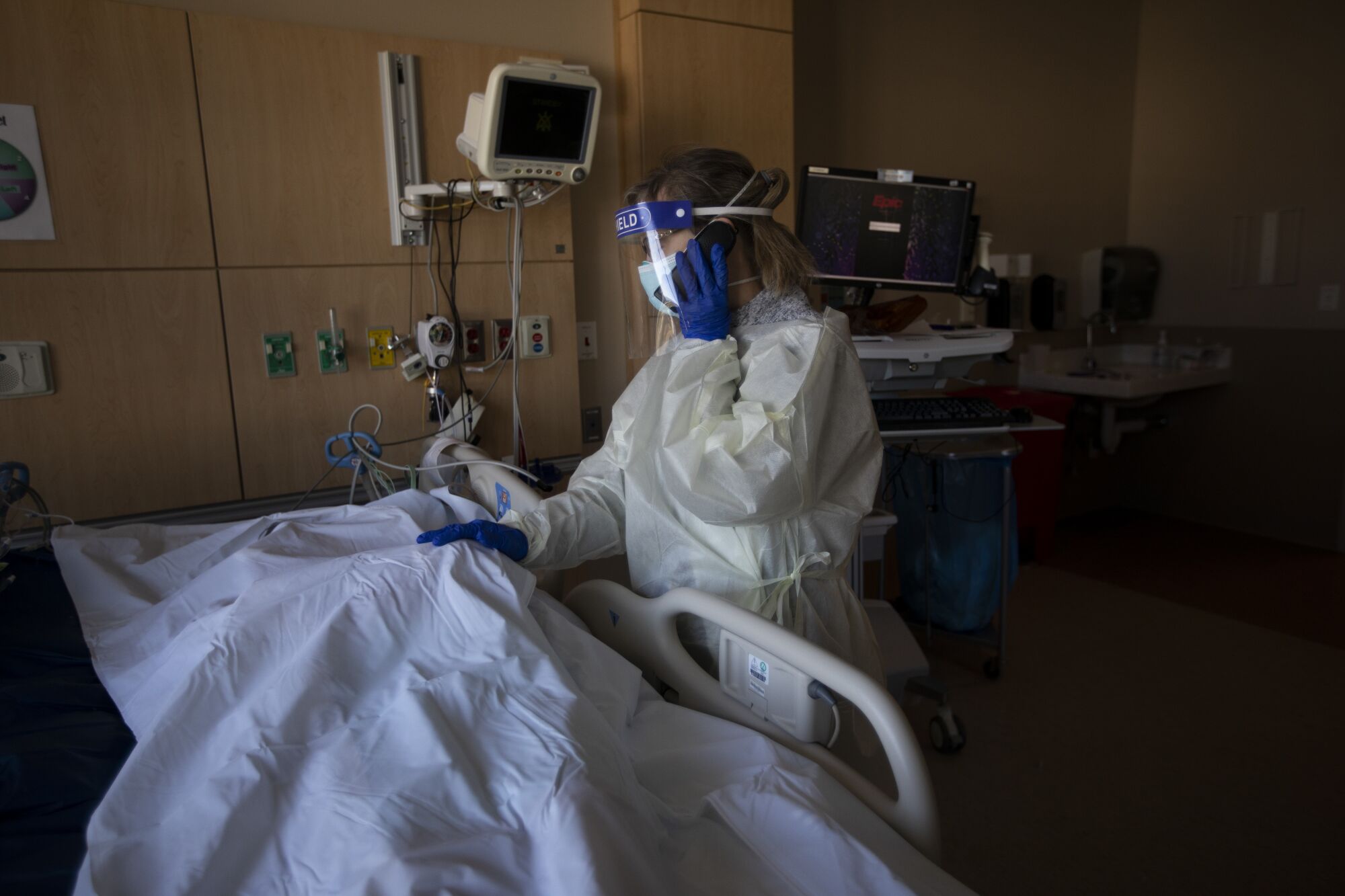 A hospital chaplain speaks one the phone next to a deceased patient covered in a sheet