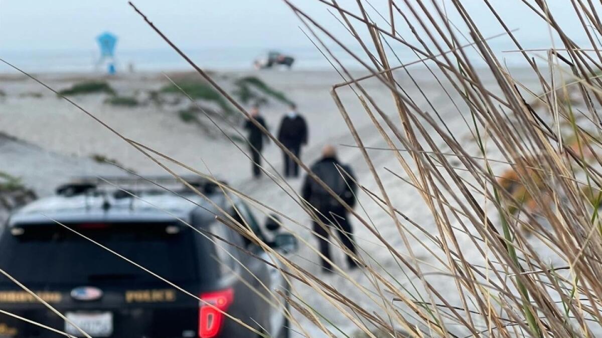 Police officers stand near a patrol SUV on a beach