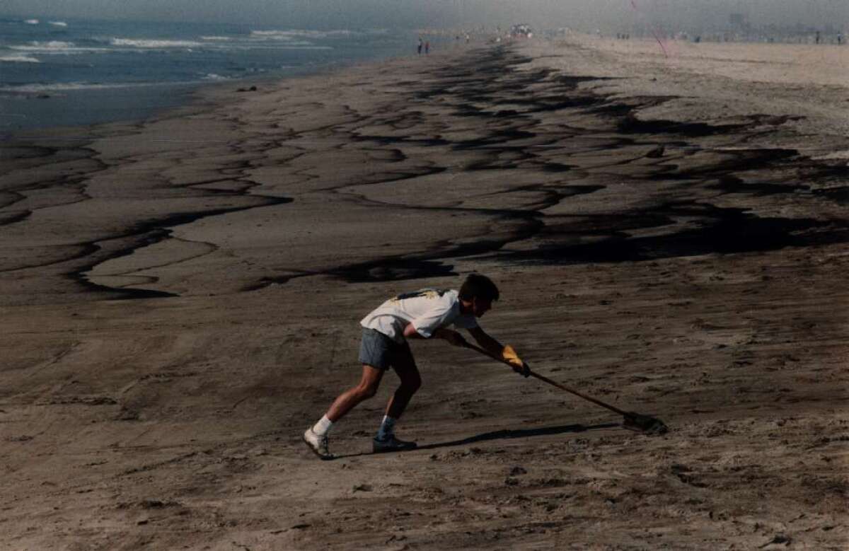 File photo from 1990 — About 400,000 gallons of crude oil from the American Trader fouled the Orange County Coast in 1990. Lance Kennedy, 15, of Newport Beach sweeps tar off Huntington Beach north of the Santa Ana River jetty during the long clean-up of the spill.