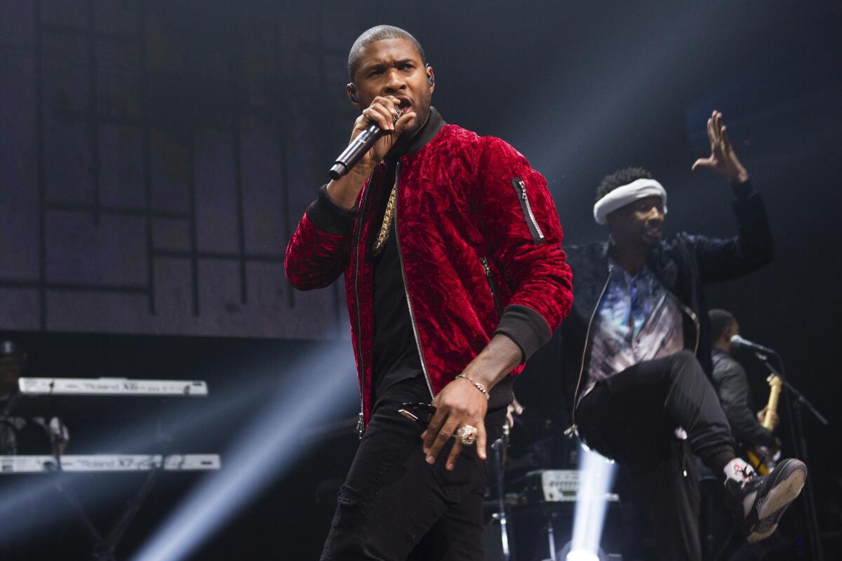 Usher wearing a red jacket and singing into a microphone on a stage