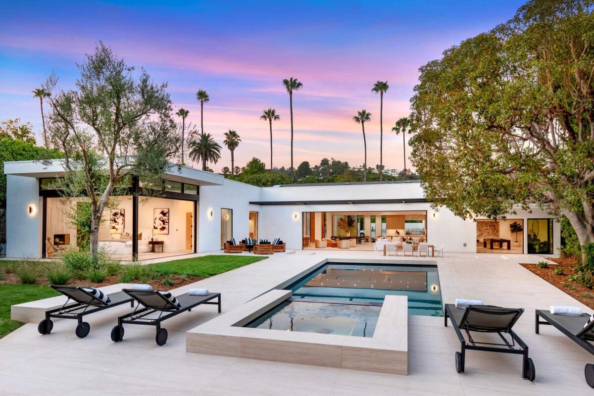 A white house with dark trim is shown with a pool in front of it