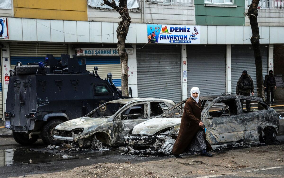 People walk past destroyed vehicles as they leave their houses during clashes in central Diyarbakir on March 15, 2016.