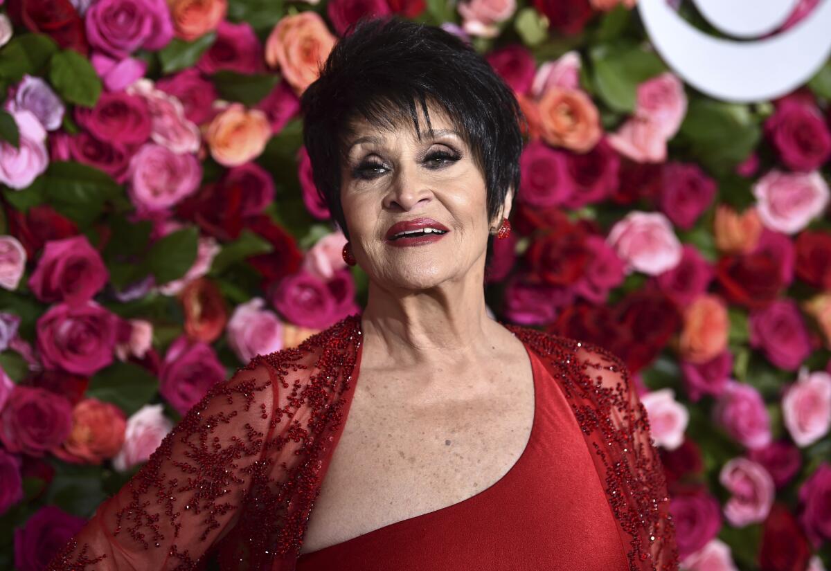 A woman in a red dress poses in front of a backdrop of roses at the Tony Awards
