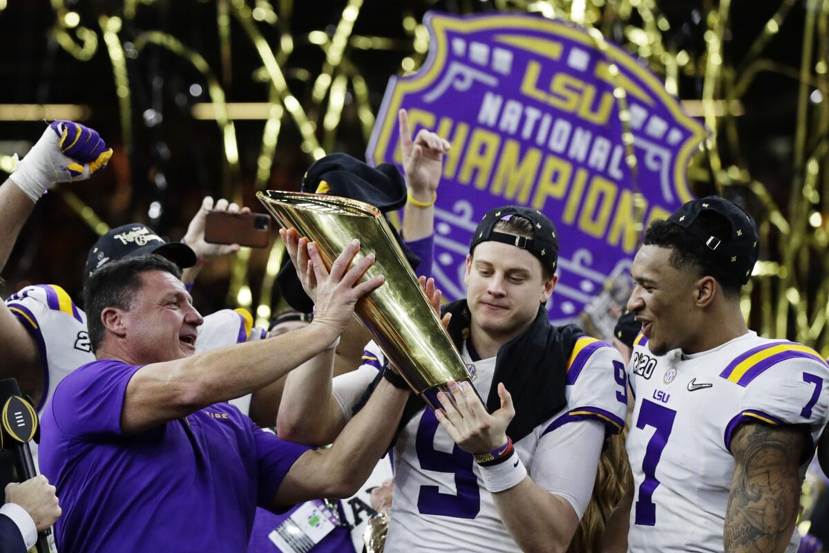 LSU coach Ed Orgeron, left, and quarterback Joe Burrow hold the CFP trophy alongside safety Grant Delpit.