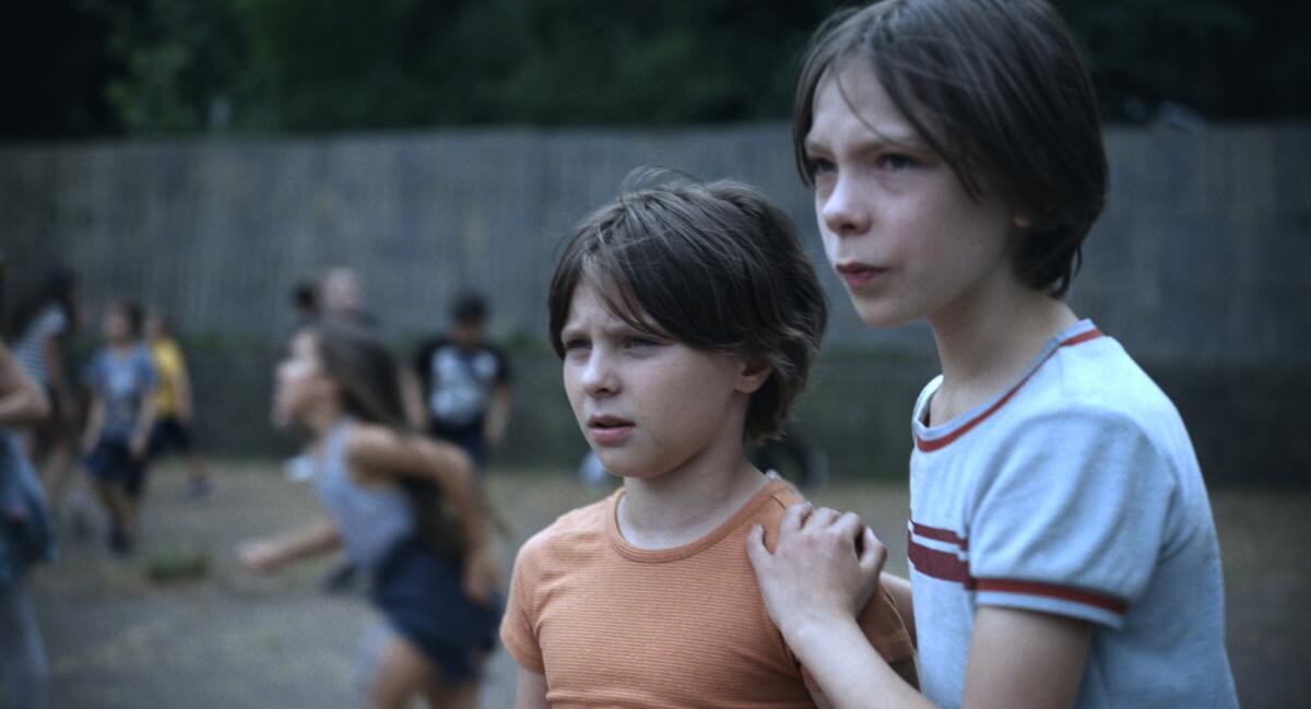 A young girl and a boy at the forefront of a schoolyard full of children playing.