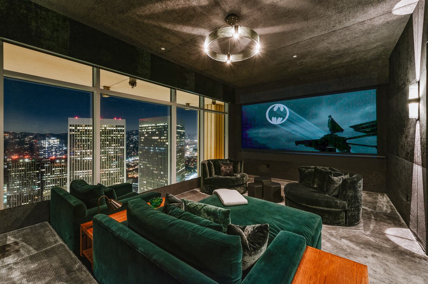 A window has an expansive city view in a room with couches and an oversized screen.