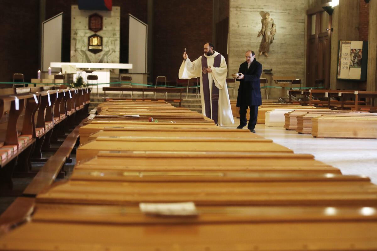 Don Marcello Crotti, left, blesses the coffins with Don Mario Carminati in the San Giuseppe church in Seriate, Italy, Saturday, March 28, 2020.