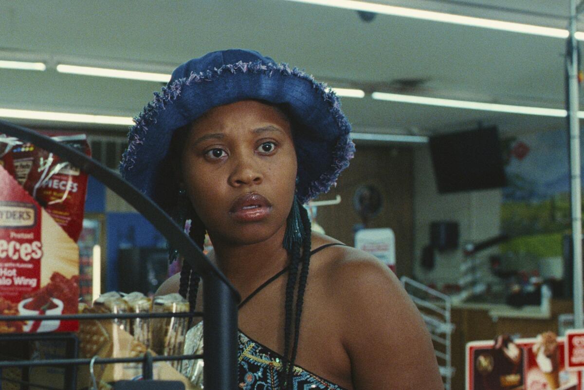 Dominique Fishback wearing a denim bucket hat stands in a convenience store in a scene from "Swarm."