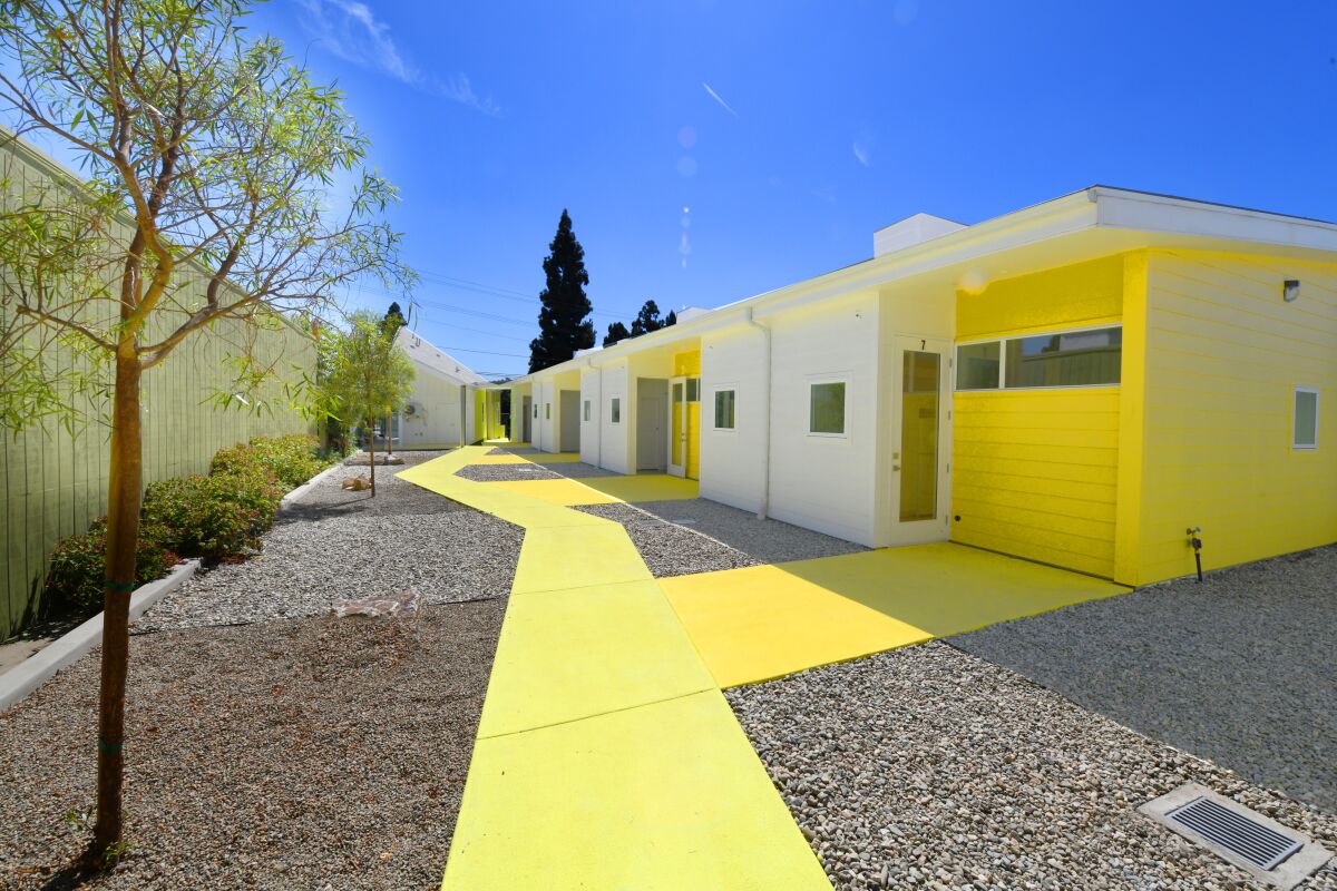 A view of a low-rise complex shows a row of small apartments in shades of yellow facing a courtyard.