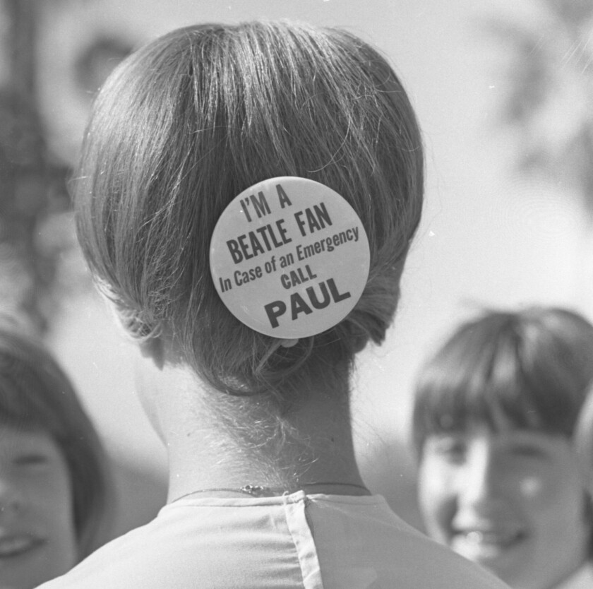 A girl is seen from behind with a round button in her hair that reads “I’m a Beatle fan. In case of an emergency call Paul.”