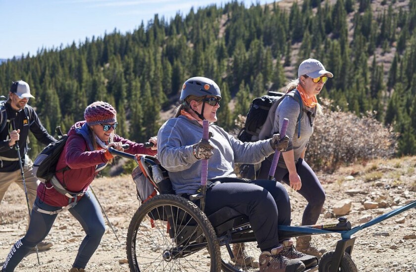 A woman who has cerebral palsy pushes the levers of a GRIT Freedom Chair to climb a mountain trail with a rope team.