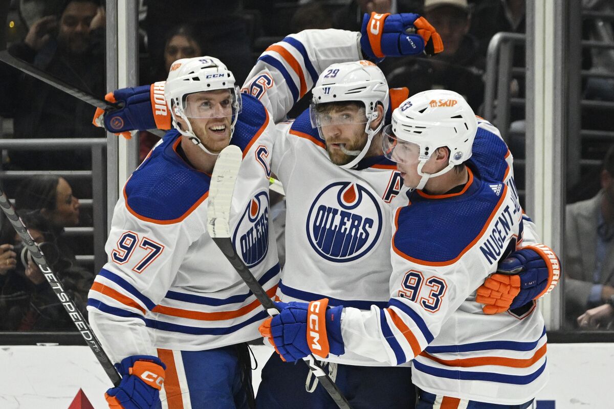 Trois joueurs de hockey en uniforme bleu, orange et blanc s'embrassent sur la glace.