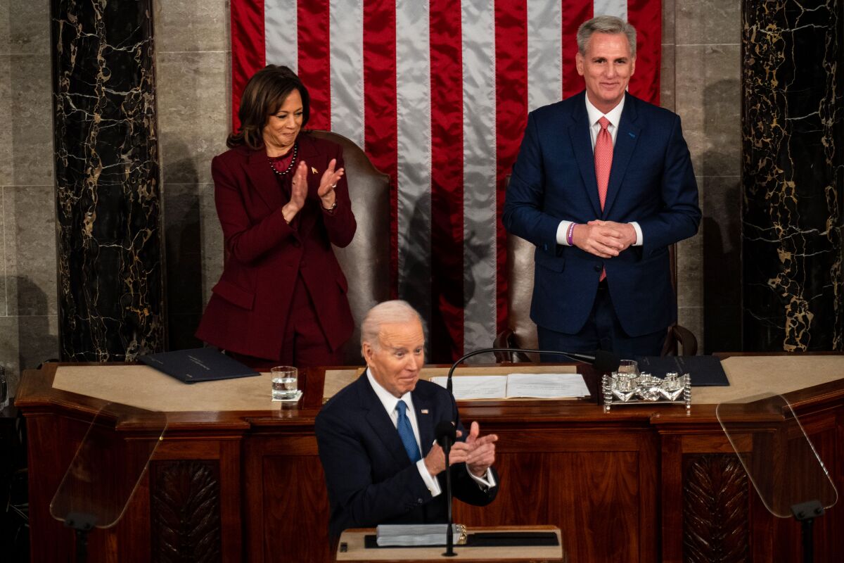 A woman and a man stand at a dais behind a speaker at a lectern