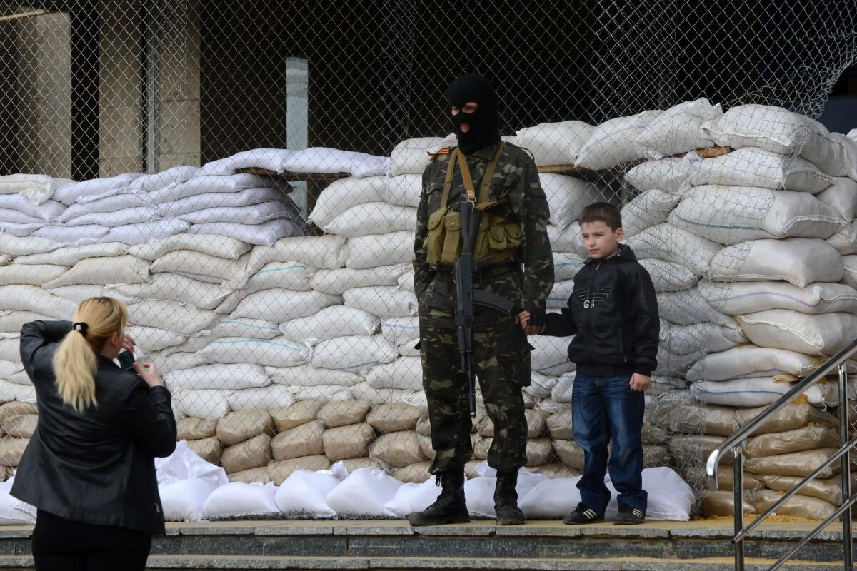 A woman takes a picture of her son standing by an armed man who is guarding a barricade outside a regional administration building in Slovyansk, Ukraine, on Sunday. Pro-Russian gunmen have seized several government buildings in eastern Ukraine.