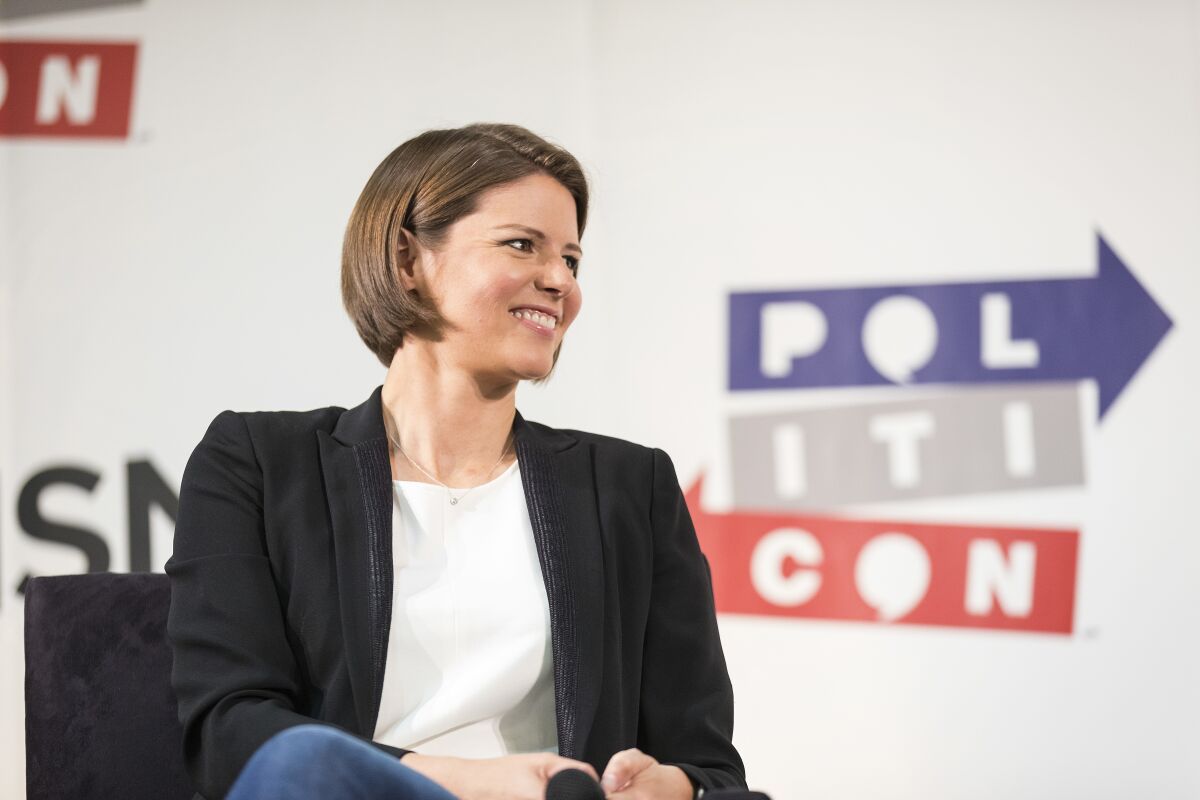 A woman with short brown hair wearing a black blazer, white shirt and jeans sitting on a panel