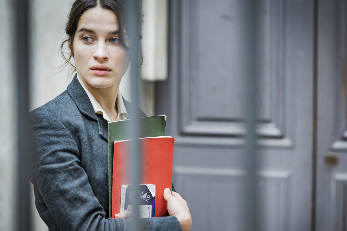 A woman stands clutching notebooks to her chest