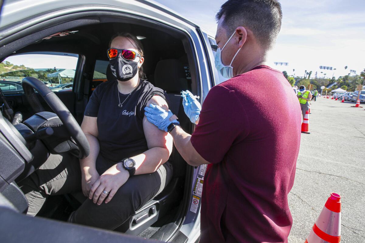 Motorist in a car receives the COVID-19 vaccine from a healthcare worker in a parking lot.