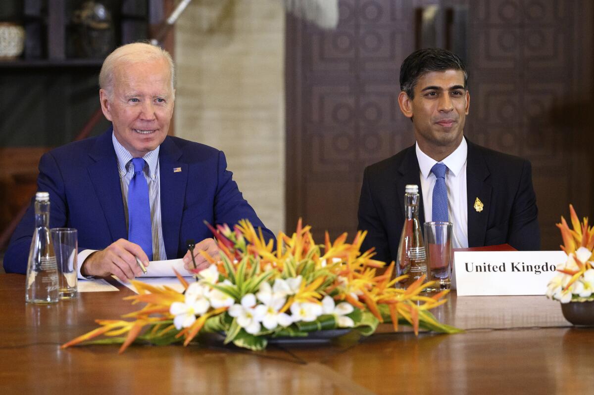 President Biden and British Prime Minister Rishi Sunak sit at a table with a floral arrangement 
