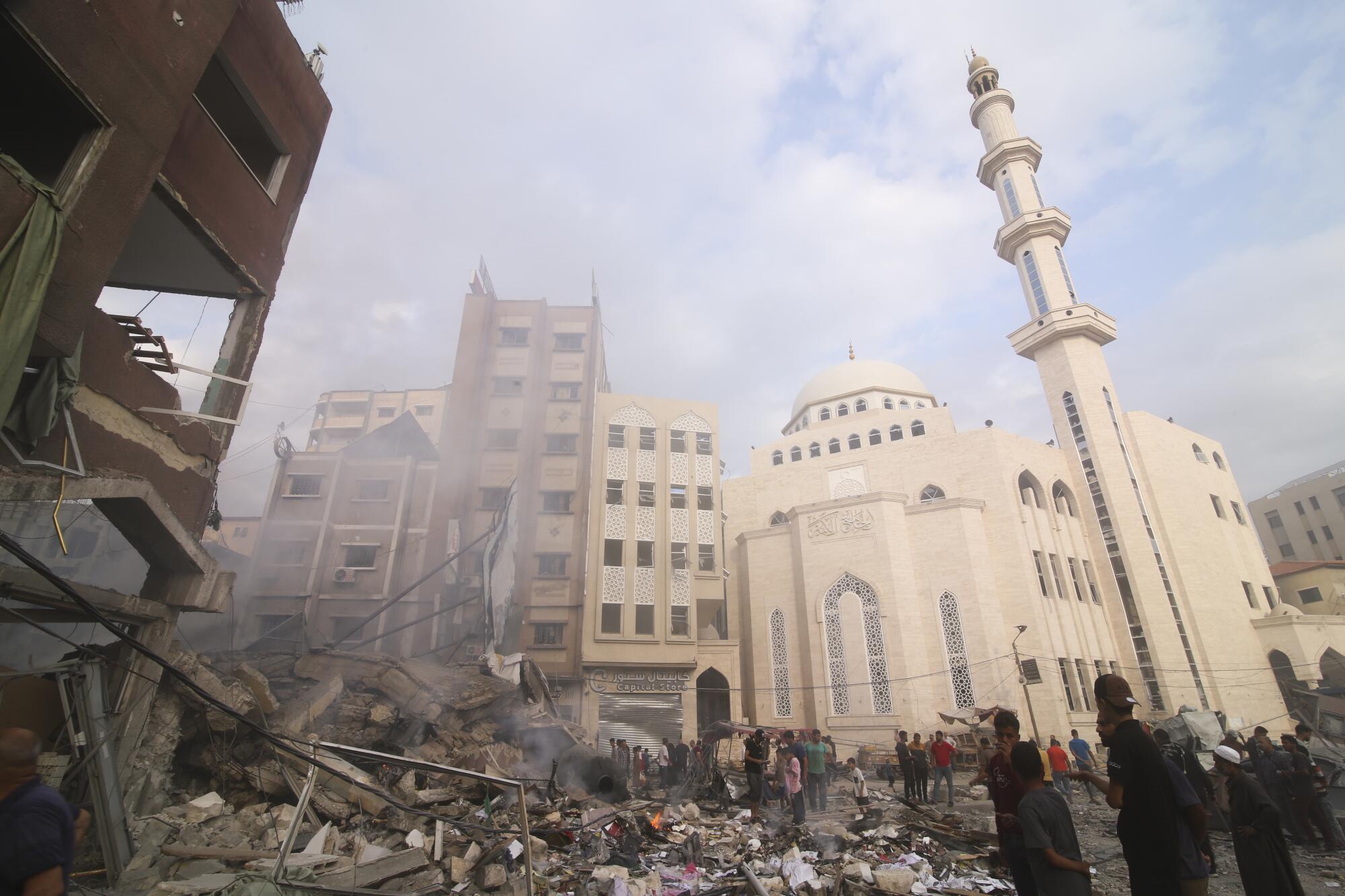 A building is reduced to rubble near a white domed mosque with a minaret and other high-rises