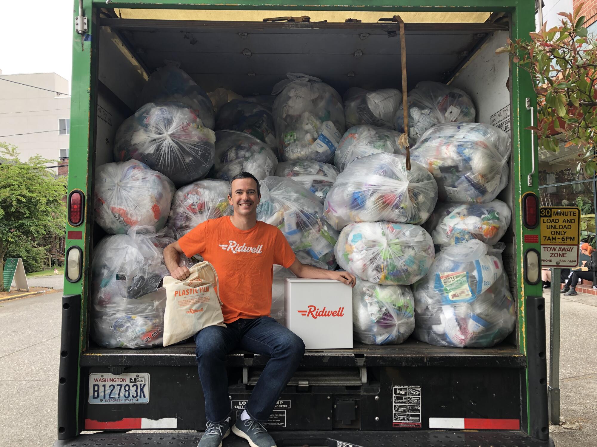 Ryan Metzger of Ridwell sits in the back of a dumpster truck loaded with plastic bags full of trash.