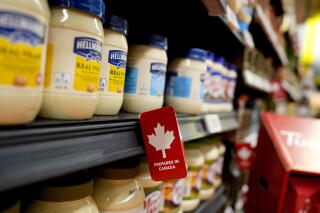 A grocery shelf lined with mayonnaise jars bears a maple leaf symbol indicating the goods were prepared in Canada.