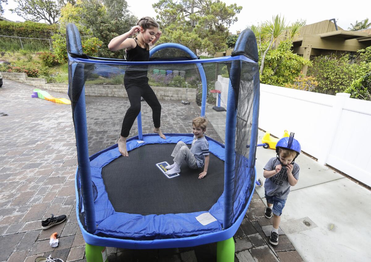 The Daniels children (from left) Ashlan, 9, Cole, 6, and Grant, 2, of El Cajon, play in the front yard of their Fletcher Hills home on Thursday with new toys purchased since they have had to stay at home because of COVID-19.
