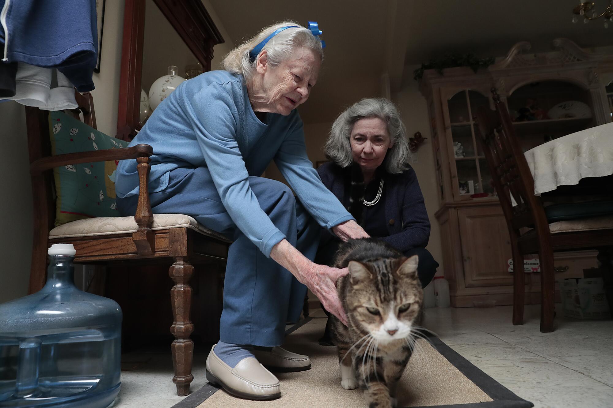 Lois Jones reaches out to her tabby cat while her daughter watches