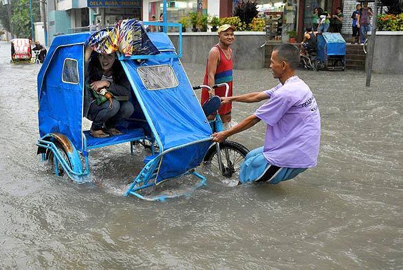 A man pulls a passenger cycle through a submerged street in suburban Manila during heavy rain brought by Typhoon Sinlaku.
