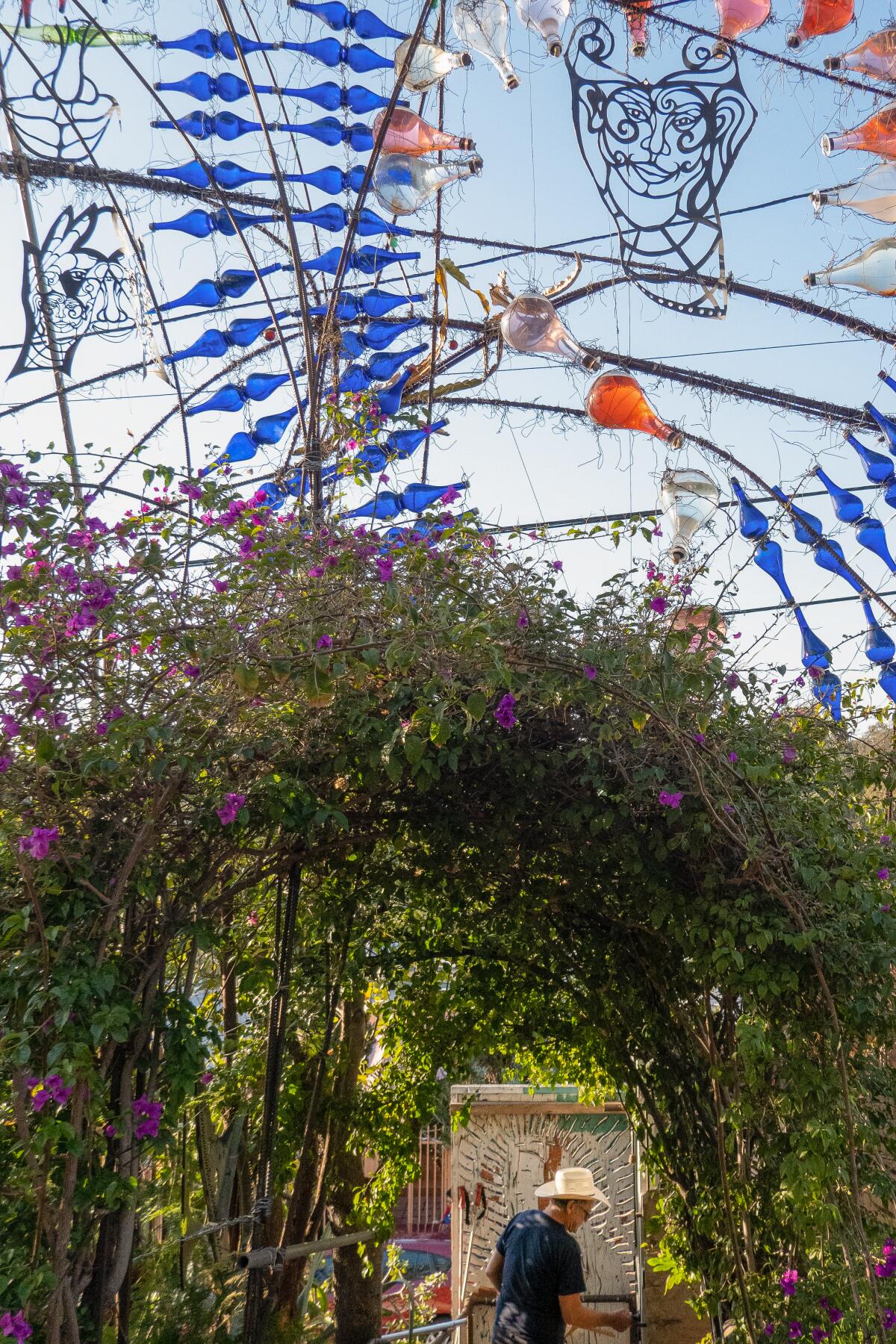 Randy King Lawrence standing by his colorful art project, framed by an archway of purple bougainvillea.