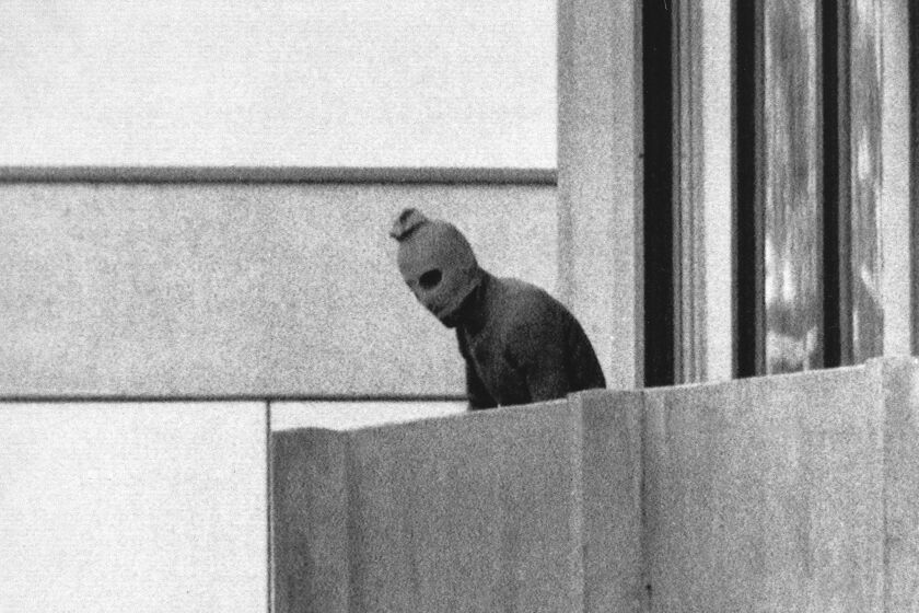 FILE - A member of the Arab Commando group which seized members of the Israeli Olympic Team at their quarters appears with a hood over his face on the balcony of the village building where the commandos held members of the Israeli team hostage, at the Munich Olympic Village, on Sept. 5, 1972. A panel of historians set up to review the 1972 attack on the Munich Olympics is starting its three-year mission to reappraise what happened before, during and after the events of five decades ago on Tuesday, the German government said. (AP Photo/Kurt Strumpf, File)