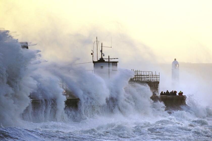 Waves crash against the sea wall and Porthcawl Lighthouse in Porthcawl, Bridgend, Wales, Britain, as Storm Eunice makes landfall Friday, Feb. 18, 2022. Millions of Britons are being urged to cancel travel plans and stay indoors Friday amid fears of high winds and flying debris as the second major storm this week prompted a rare “red” weather warning across southern England. ( Jacob King/PA via AP)